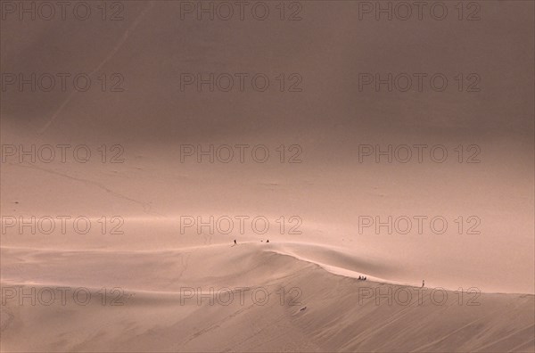 CHINA, Gansu, Dunhuang, Sand dunes with people standing on the ridge in the distance