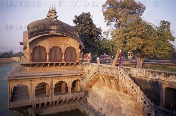 INDIA, Rajasthan , Deeg , "Gopal Bhavan, the Suraj Mahl’s Palace built in the 18th C in Rajput and Mughal style.  Women carrying large jars on their heads across stone wall."