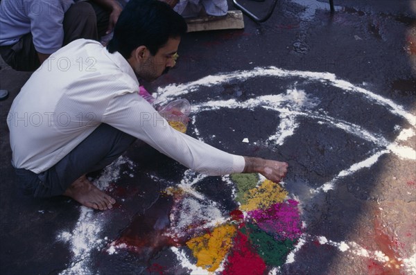 INDIA, Delhi , Man painting wheel-like design on the ground to be used as a base for a bonfire during the Holi Festival.