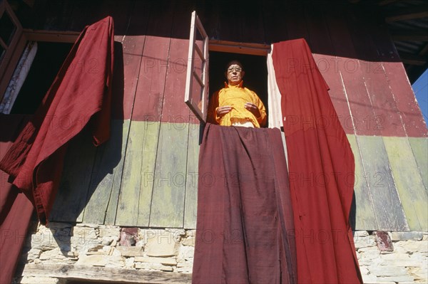 INDIA, Sikkim, Pemayangste Monastery, Buddhist Lama standing at a window with drapes hanging from the open window frames.