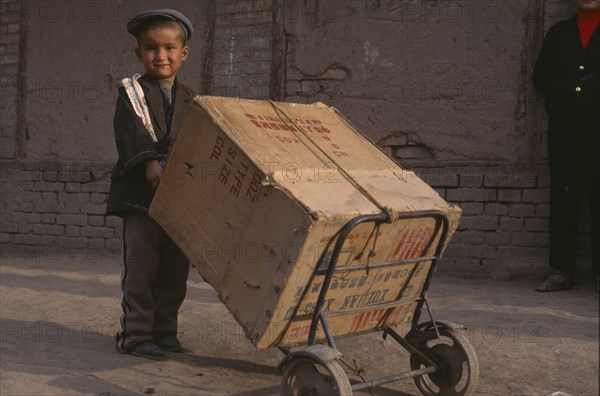 CHINA, Xinjiang, Kashgar , Child pushing a box on two wheeled trolley