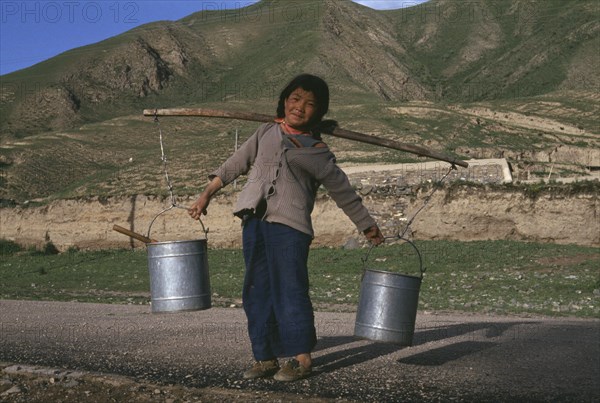 CHINA, Gansu Provence, Xiahe , Child carrying water buckets on the ends of a stick over sholders.