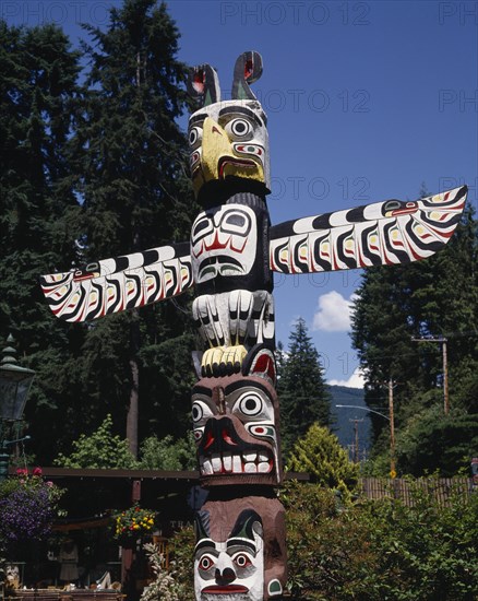CANADA, British Columbia, Vancouver, Stanley Park a close up of the top of a Totem pole with gardens behind