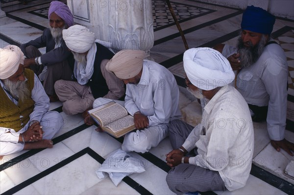 INDIA, Punjab, Amritsar, Group of Sikh men reading from holy book on black and white marble floor of the Golden Temple complex.