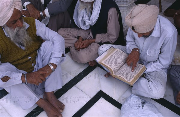 INDIA, Punjab, Amritsar, Group of elderly men reading Sikh holy book at Golden Temple sitting on black and white marble floor..
