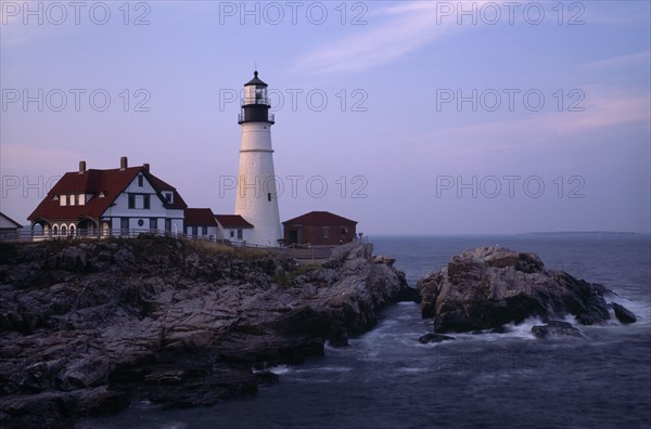 USA, Maine, Portland, Portland Head Lighthouse. Waves crashing against rocks seen at dusk in warm light.