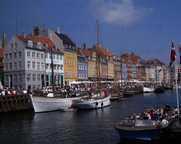 DENMARK, Zealand, Copenhagen, Nyhavn Harbour. Traditional waterfront buildings and tourists traveling along waterway on boats