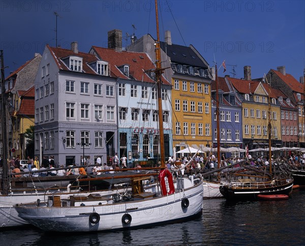 DENMARK, Zealand, Copenhagen, Nyhavn Harbour. Traditional waterfront buildings with crowds of tourists and moored boats on water
