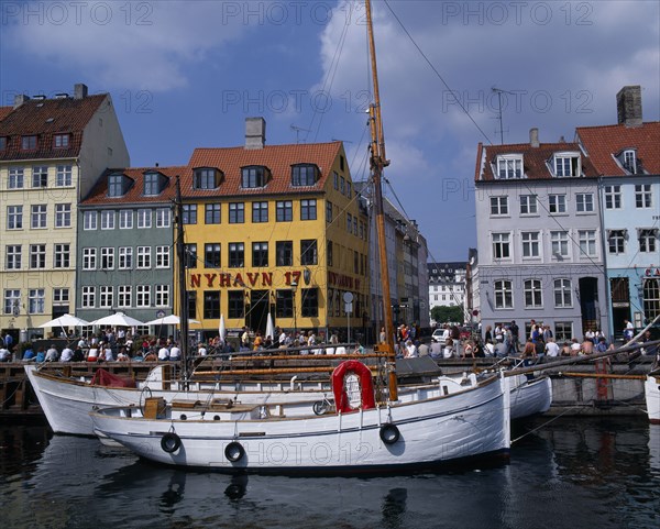 DENMARK, Zealand, Copenhagen, Nyhavn Harbour. Traditional waterfront buildings with groups of tourists and moored boats on water