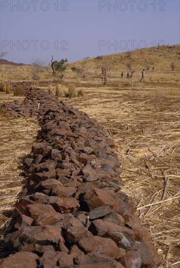 Burkina Faso, Environment, Flooding, "Bund, low rock walls built to prevent soil erosion by flash floods. Stones are placed along the contours on gentle slopes. Sometimes the bunds are reinforced by planting tough grasses along the lines. The stones and grass encourage rain water to infiltrate the soil and reduce the amount of rain water that is lost by run-off. Any soil that has been eroded by run-off is trapped by the bund. Topsoil and organic matter (e.g. leaf litter) is deposited here.Bunds are placed 10 to 25 metres apart"