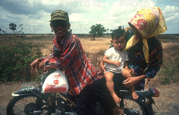 CAMBODIA, Kompong Thom, National Route 6.  Motorbike rider with woman and baby on pillion.