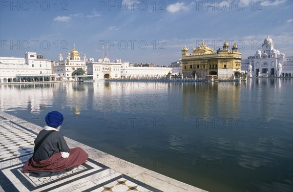 INDIA, Punjab, Amritsar , Sikh man sitting on marble walkway beside the sacred pool surrounding the Golden temple