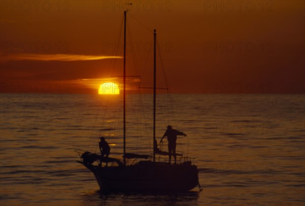 10045658 LEISURE Sailing Yachting Two people seen on a sailing boat at sunset with red sky and a low sun. Borth  Wales  UK