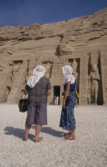 EGYPT, Abu Simnel , Two female tourists wearing head scarves in front of staues of Ramesses II at the temple entrance