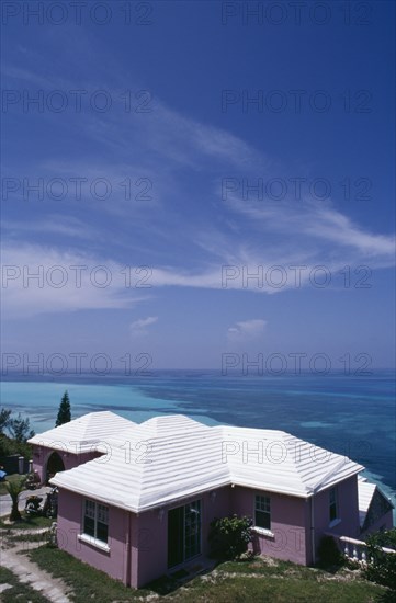 BERMUDA, Somerset, Clifftop house. Purple painted exterior with white roof and view out to sea.  Windswept cloud in blue sky overhead.