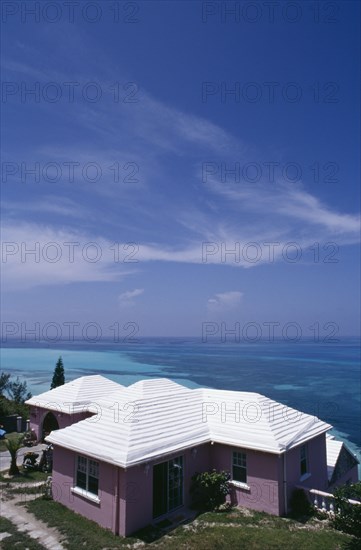 BERMUDA, Somerset, Clifftop house. Purple painted exterior with white roof and view out to sea. Windswept cloud in blue sky overhead.