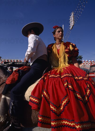 SPAIN, Andalucia, Seville, Couple in Flamenco costume riding horseback at the April Fair in Los Remedios district