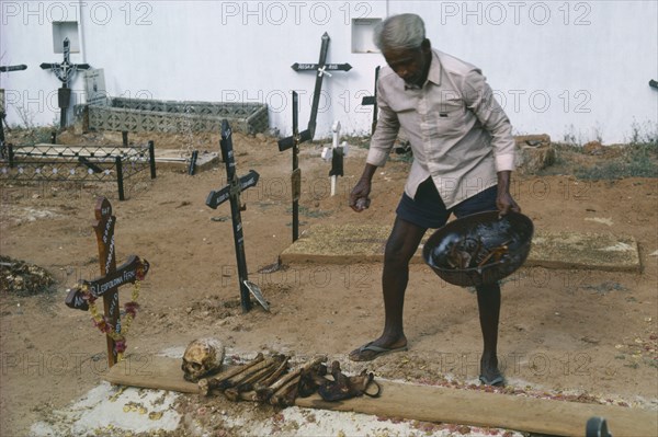 INDIA, Goa, Colva, Man cleaning bones at family grave. The bones are removed and washed to make space for the next family member