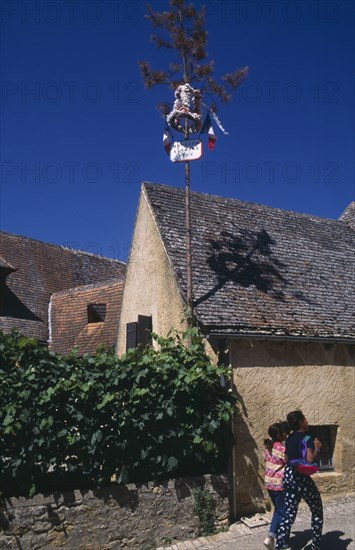 FRANCE, Aquitaine, Dordogne,  La Roque. Easter decorations attached to pole on exterior of house with two young girls walking past