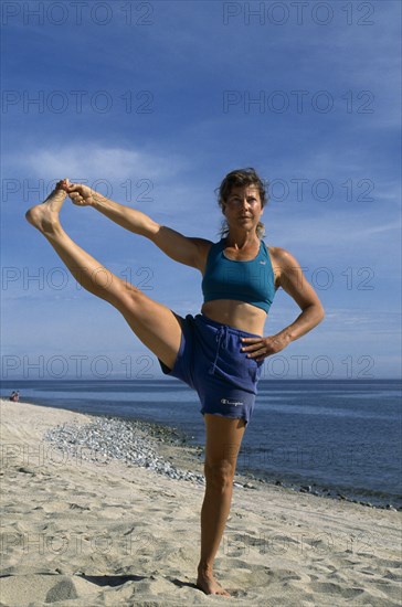 10048200 SPORT Excercise Yoga Woman performing a yoga pose on a sandy beach
