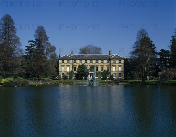 ENGLAND, London, Kew Gardens, View over lake towards large house and fountains with visitors sitting on the banks.