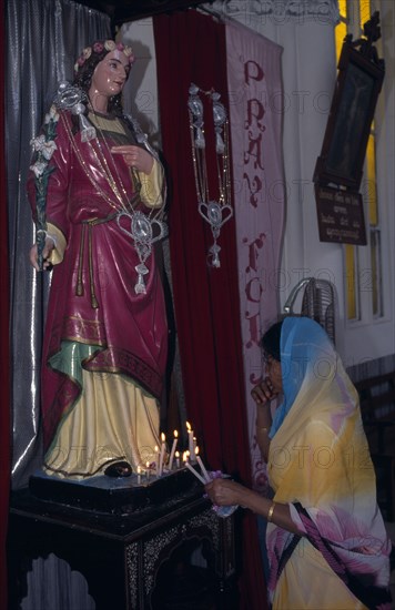 INDIA, Karnataka, Mysore, Indian woman lighting candles in front of statue of religious figure at Christmas.