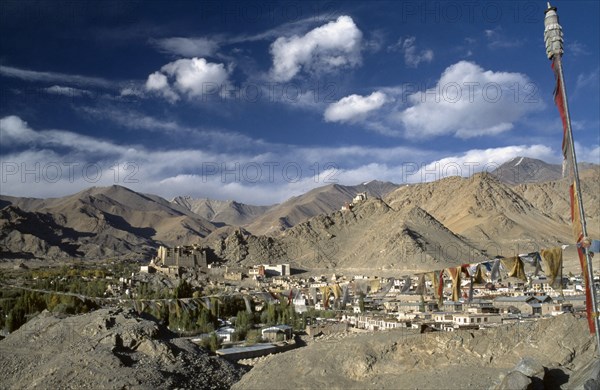 INDIA, Ladakh, Leh Valley , Prayer flags hanging above village set in mountainous landscape with hilltop palace in the distance