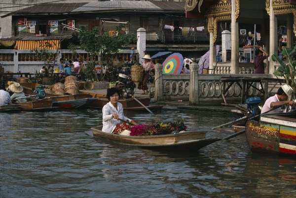 THAILAND, Bangkok, Floating Market, Woman rowing canoe containing flowers with woman on the jetty behind loading boat with wicker baskets.