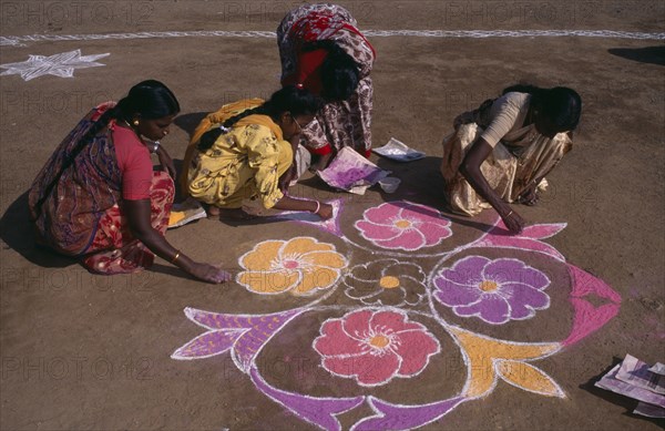 INDIA, Tamil Nadu, Pongal Festival.  Four day festival to mark the end of harvest.  Women painting decorative floral pattern on ground using coloured powder dyes.