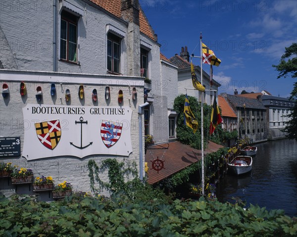 BELGIUM, West Flanders, Bruges, "Boat house with a sign for excursions, Different countries flags painted onto clogs. Boats docked on the canal, and flags flying."