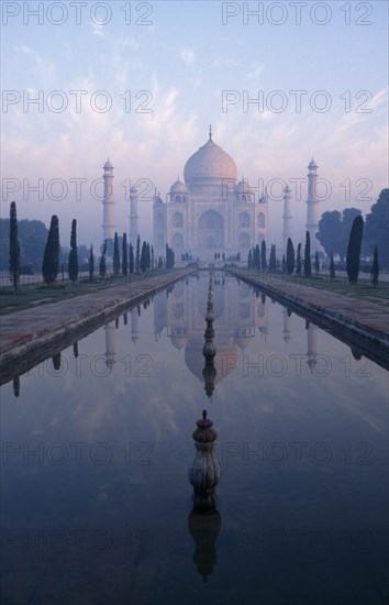 INDIA, Uttar Pradesh, Agra , Taj Mahal reflected in watercourse through formal gardens in pale pink dawn mist.