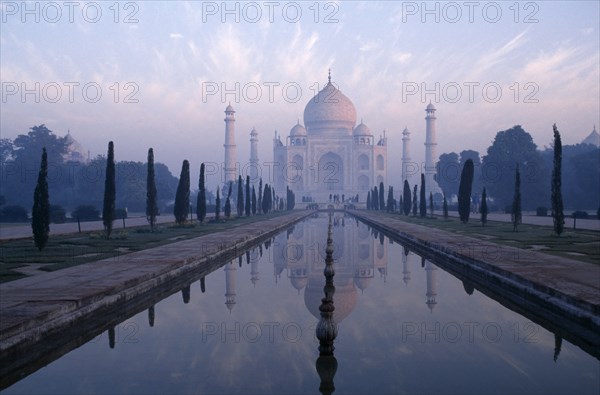 INDIA, Uttar Pradesh, Agra, The Taj Mahal exterior reflected in watercourse through formal gardens in pale pink dawn mist.