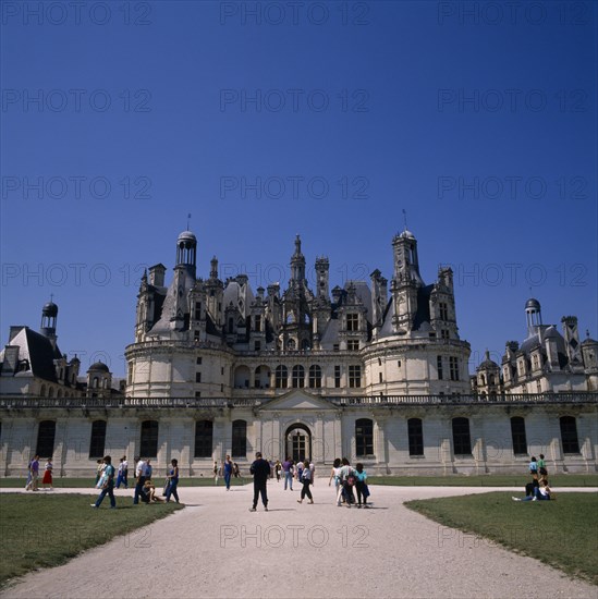 FRANCE, Loire Valley, Loir et Cher, Chambord Chateau. Tourists on gravelled entrance between green lawns. Blue sky