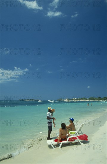 WEST INDIES, Jamaica, Negril, Man selling lobster to tourists on beach sitting on sun loungers by the water