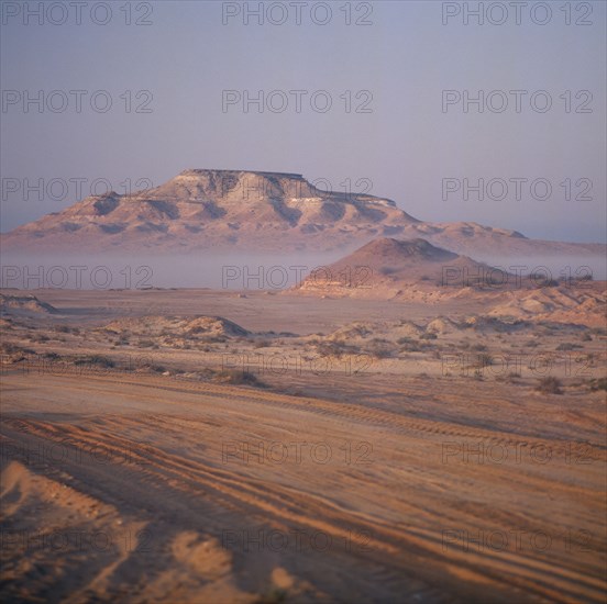 UAE, Abu Dhabi, "Nr Ruwais, Desert and hills with vehicle tracks on flat area in foreground seen on a Misty morning "