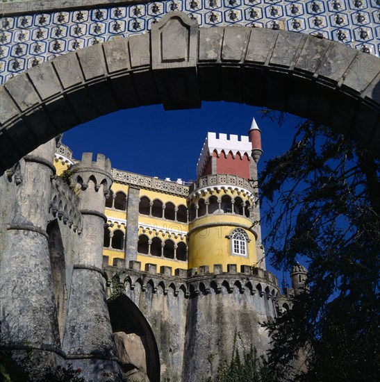 PORTUGAL, Estremadura, Sintra, Pena Palace. View through archway to yellow and red tower with arches and crennalations