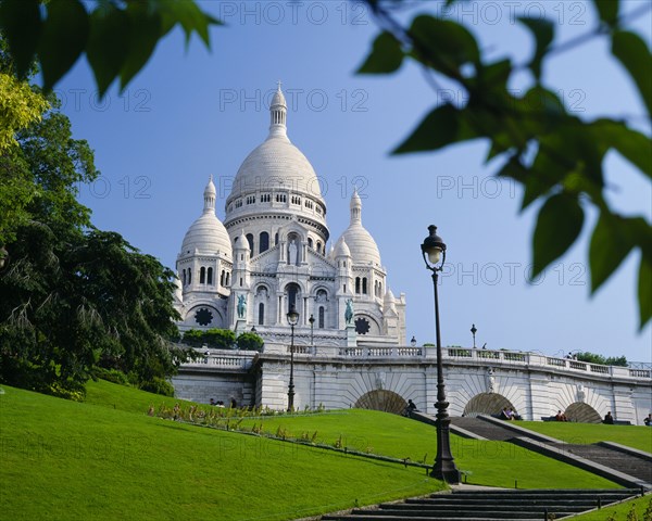 FRANCE, Ile de France, Paris, Sacre Coeur.  Exterior against blue sky partly framed by tree branches.