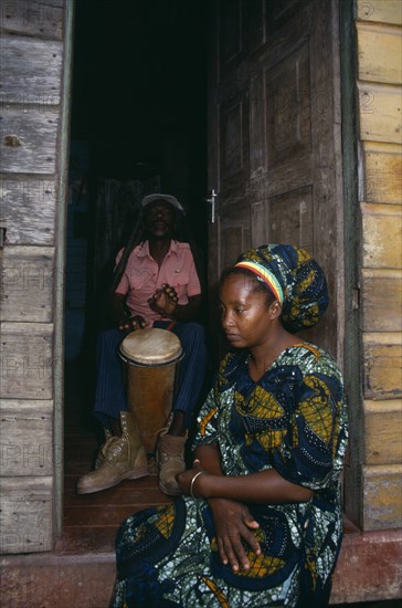 JAMAICA, Music, Percussion, Rastafarian couple with man playing bongo drums inside home while woman sits in open doorway.