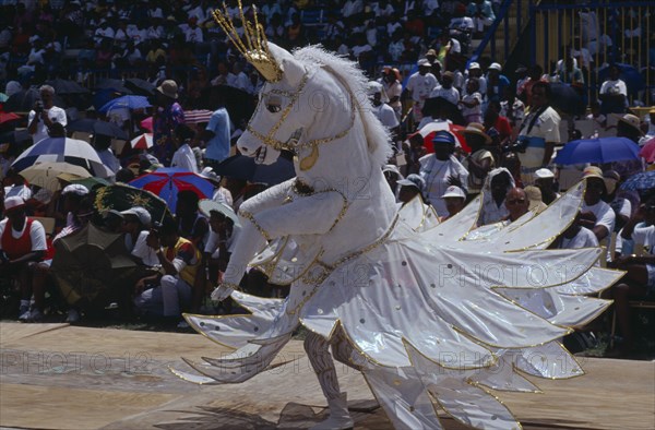 WEST INDIES, Barbados, Crop Over festival celebrating the sugar cane harvest with reveller dressed in horse costume parading in front of crops.