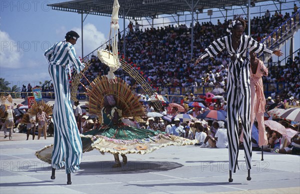WEST INDIES, Barbados, Festivals, Crop Over sugar cane harvest festival.  Grand Kadooment carnival parade stilt walkers in striped costume.