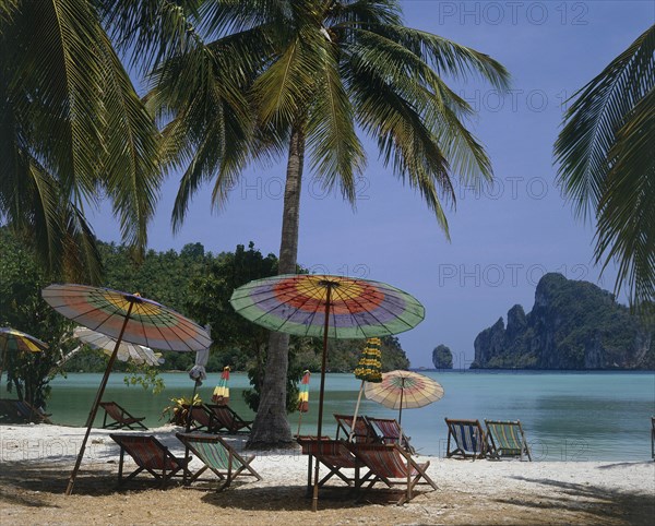 THAILAND, Krabi, Phi Phi Island, Beach in enclosed bay with deckchairs and umbrellas beneath coconut palm trees