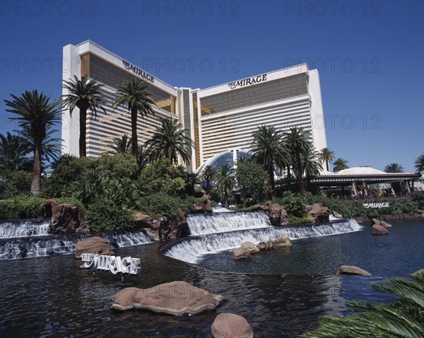 USA, Nevada, Las Vegas, Mirage Hotel and Casino. View across waterfall and palm tree lined rock pool to hotel entrance.