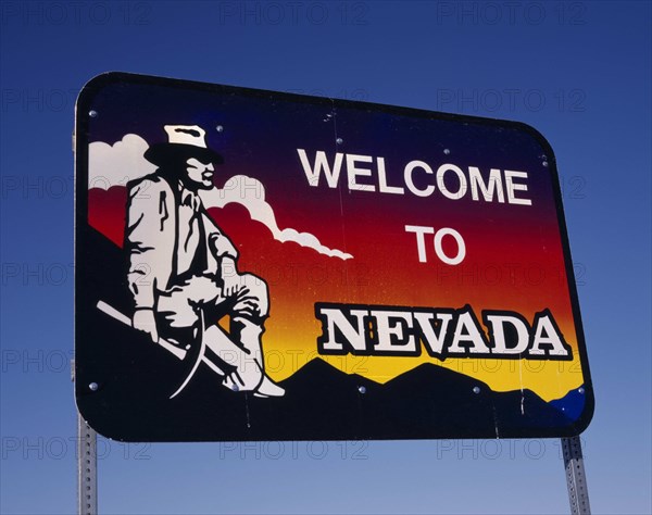 USA, Nevada, Welcome to Nevada roadsign with gold-digger looking across towards mountains and clouds at sunset