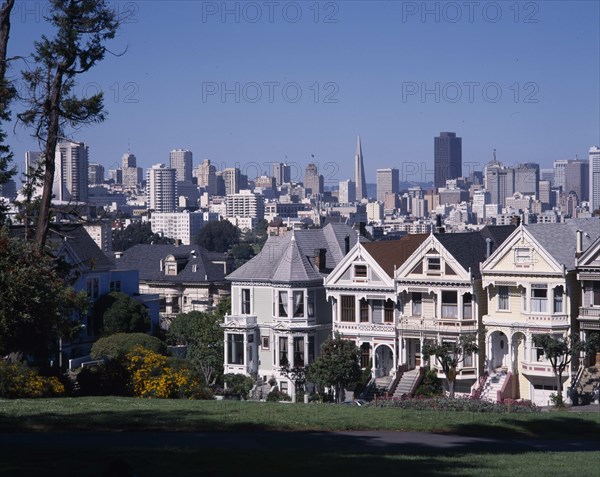 USA, California, San Fransisco, Alamo Square with city skyline beyond a row of timber town houses with steps leading up to doorways