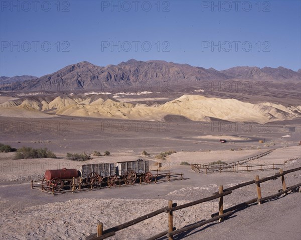 USA, California, Death Valley, Historic Harmony Borax Works. Wooden containers and steel cylinder on trailers in fenced area in desert landscape with hills in the background