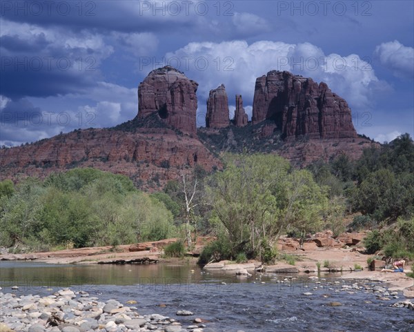 USA, Arizona, Sedona, Cathedral Rock in Oak Creek Canyon. View over river to wind eroded rock formation with a girl and boy playing at waters edge.