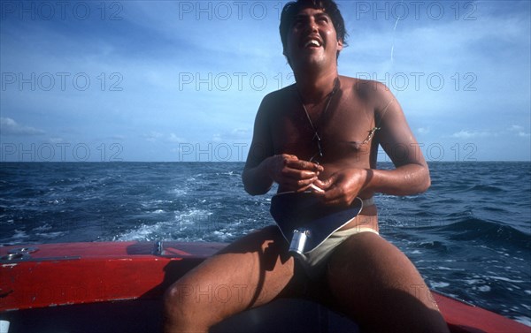CUBA, Ciego de Avila, Cayo Guillermo, Man sitting at the back of a boat putting bait on the end of a fishing hook