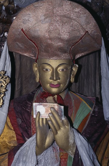 INDIA, Ladakh, "Buddhist temple statue of high ranking lama with money placed in its hands and draped with white, silk kata as mark of esteem."