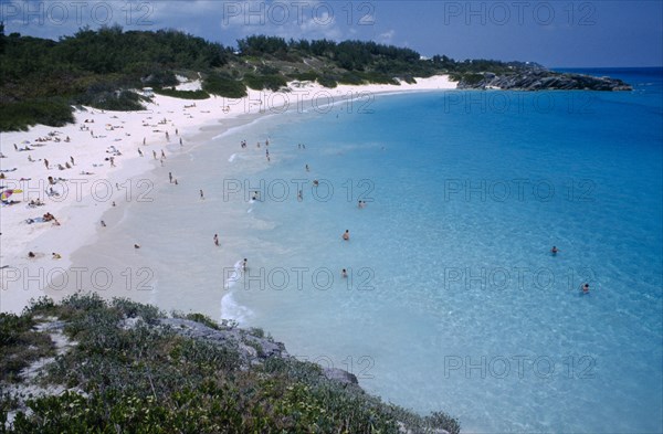 BERMUDA, Southampton, Horseshoe Bay, View over bay lined by sandy beach and vegetation with people sunbathing and in the water.