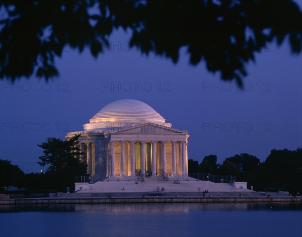 USA, Washington DC, Jefferson Memorial illuminated at night with a lake in the foreground seen through the branches of a tree